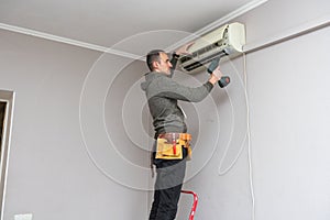 Professional electrician man with screwdriver maintaining, cleaning modern air conditioner indoors. Young technician