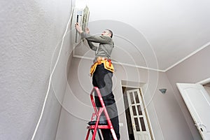 Professional electrician man with screwdriver maintaining, cleaning modern air conditioner indoors. Young technician