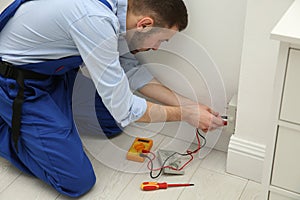 Professional electrician with tester checking voltage indoors