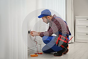 Professional electrician with tester checking voltage in room