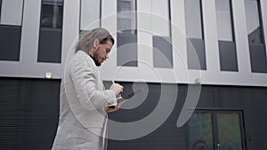 Professional employee writing typing on tablet using stylus while walking near the office building