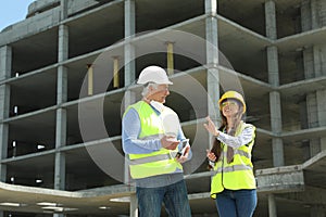 Professional engineer and foreman with tablet in safety equipment at construction site