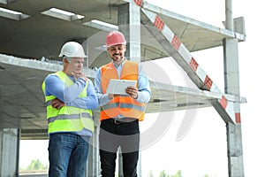 Professional engineer with tablet and foreman in safety equipment at construction site