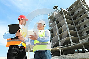 Professional engineer with tablet and foreman in safety equipment at construction site