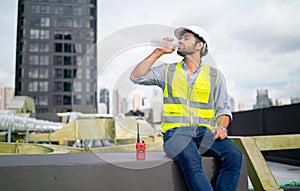 Professional engineer or technician worker man drink water from bottle and sit in area of terrace of construction site