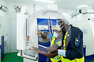 Professional engineer wearing a hard hat and safety glasses operating CNC milling machine in manufacturing workshop