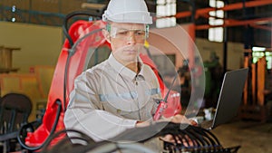 Professional engineer wearing safety helmet and glasses, holding laptop standing in the robotic arm manufacturing industrial.