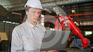 Professional engineer wearing safety helmet and glasses, holding laptop standing in the robotic arm manufacturing industrial.