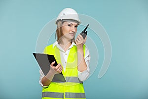Professional engineer. A woman in a hardhat and bright jelly using a tablet and a walkie-talkie, on a blue background