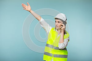 Professional engineer. A woman in a protective helmet and a bright vest gives instructions on a walkie-talkie, on a blue