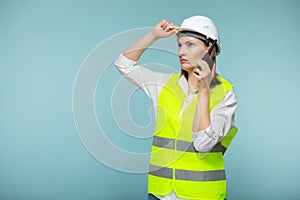 Professional engineer. A woman in a protective helmet and a bright vest gives instructions on a walkie-talkie, on a blue