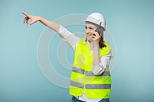 Professional engineer. A woman in a protective helmet and a bright vest gives instructions on a walkie-talkie, on a blue