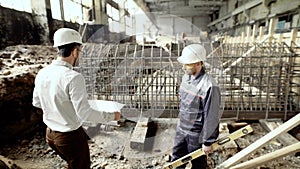 Professional engineers working together on construction site. Chief architect walking to worker standing near formwork