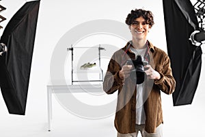 Professional european photographer man holding photo camera posing smiling to camera standing in photostudio