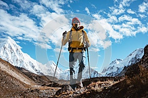Professional expeditor with trekking sticks and traveling backpack going by mountains tack. Solo tourist hiking across high snowy