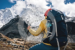 Professional expeditor with trekking sticks and traveling backpack going by mountains tack. Solo tourist hiking across high snowy