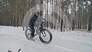 Professional extreme sportsman biker sit a fat bike in outdoor. Cyclist recline in the winter snow forest. Man walk with