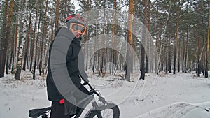 Professional extreme sportsman biker sit a fat bike in outdoor. Cyclist recline in the winter snow forest. Man walk with