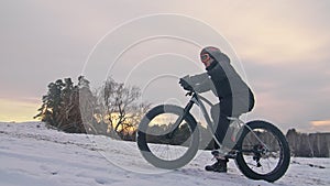 Professional extreme sportsman biker sit a fat bike in outdoor. Cyclist recline in the winter snow forest. Man walk with