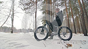 Professional extreme sportsman biker sit a fat bike in outdoor. Cyclist recline in the winter snow forest. Man walk with