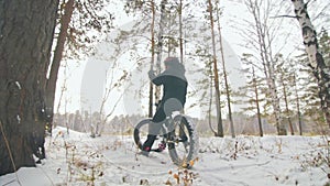 Professional extreme sportsman biker sit a fat bike in outdoor. Cyclist recline in the winter snow forest. Man walk with