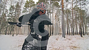 Professional extreme sportsman biker sit a fat bike in outdoor. Cyclist recline in the winter snow forest. Man walk with