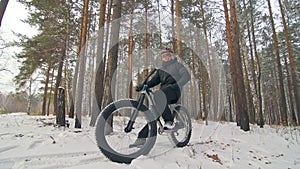 Professional extreme sportsman biker sit a fat bike in outdoor. Cyclist recline in the winter snow forest. Man walk with