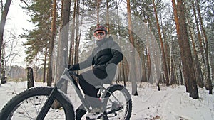 Professional extreme sportsman biker sit a fat bike in outdoor. Cyclist recline in the winter snow forest. Man walk with