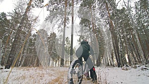 Professional extreme sportsman biker sit a fat bike in outdoor. Cyclist recline in the winter snow forest. Man walk with