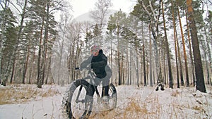 Professional extreme sportsman biker sit a fat bike in outdoor. Cyclist recline in the winter snow forest. Man walk with