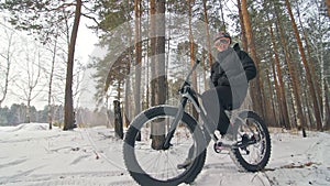 Professional extreme sportsman biker sit a fat bike in outdoor. Cyclist recline in the winter snow forest. Man walk with