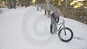 Professional extreme sportsman biker sit a fat bike in outdoor. Cyclist recline in the winter snow forest. Man walk with