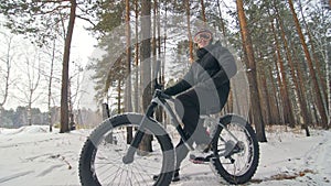 Professional extreme sportsman biker sit a fat bike in outdoor. Cyclist recline in the winter snow forest. Man walk with