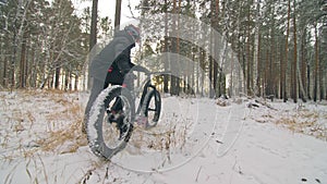 Professional extreme sportsman biker stand a fat bike in outdoor. Cyclist recline in the winter snow forest. Man walk