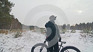 Professional extreme sportsman biker stand a fat bike in outdoor. Cyclist recline in the winter snow forest. Man walk