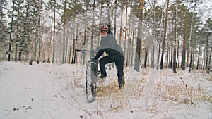 Professional extreme sportsman biker stand a fat bike in outdoor. Cyclist recline in the winter snow forest. Man walk