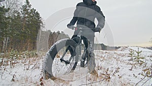 Professional extreme sportsman biker stand a fat bike in outdoor. Cyclist recline in the winter snow forest. Man walk