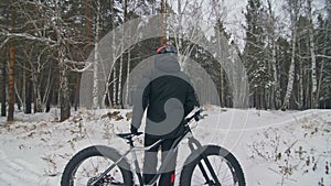 Professional extreme sportsman biker stand a fat bike in outdoor. Cyclist recline in the winter snow forest. Man walk