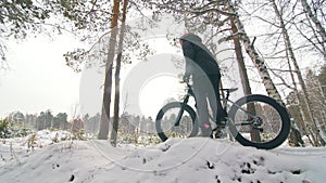 Professional extreme sportsman biker stand a fat bike in outdoor. Cyclist recline in the winter snow forest. Man walk