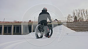 Professional extreme sportsman biker stand a fat bike in outdoor. Cyclist recline in the winter snow forest. Man walk