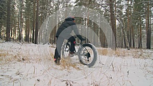 Professional extreme sportsman biker stand a fat bike in outdoor. Cyclist recline in the winter snow forest. Man walk