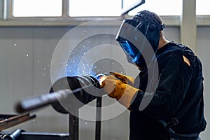 Professional factory technologies. Man welding in uniform and helmet.