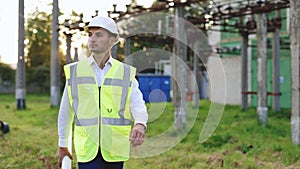 Professional Factory Worker Wearing Hard Hat Holds Paper Plan, Walking Through Modern Industrial Electric Station