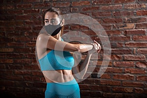 Professional female athlete training on brick wall background wearing face mask. Sport during quarantine