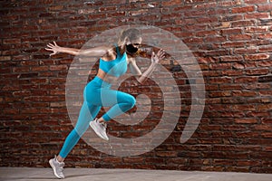 Professional female athlete training on brick wall background wearing face mask. Sport during quarantine