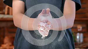 Professional female baker or housewife clapping hands and flour flying, slow-motion in home kitchen