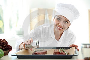 Professional female chef preparing meat on table