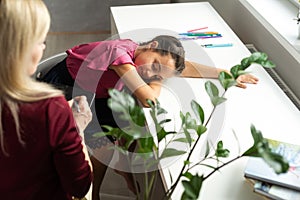 Professional female child psychologist working with a little preschool girl in a bright office. Woman makes notes