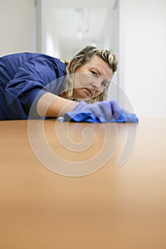 Professional female cleaner wiping table in office