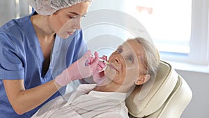 Professional female cosmetologist doing face contouring injections to senior woman in aesthetic medicine office